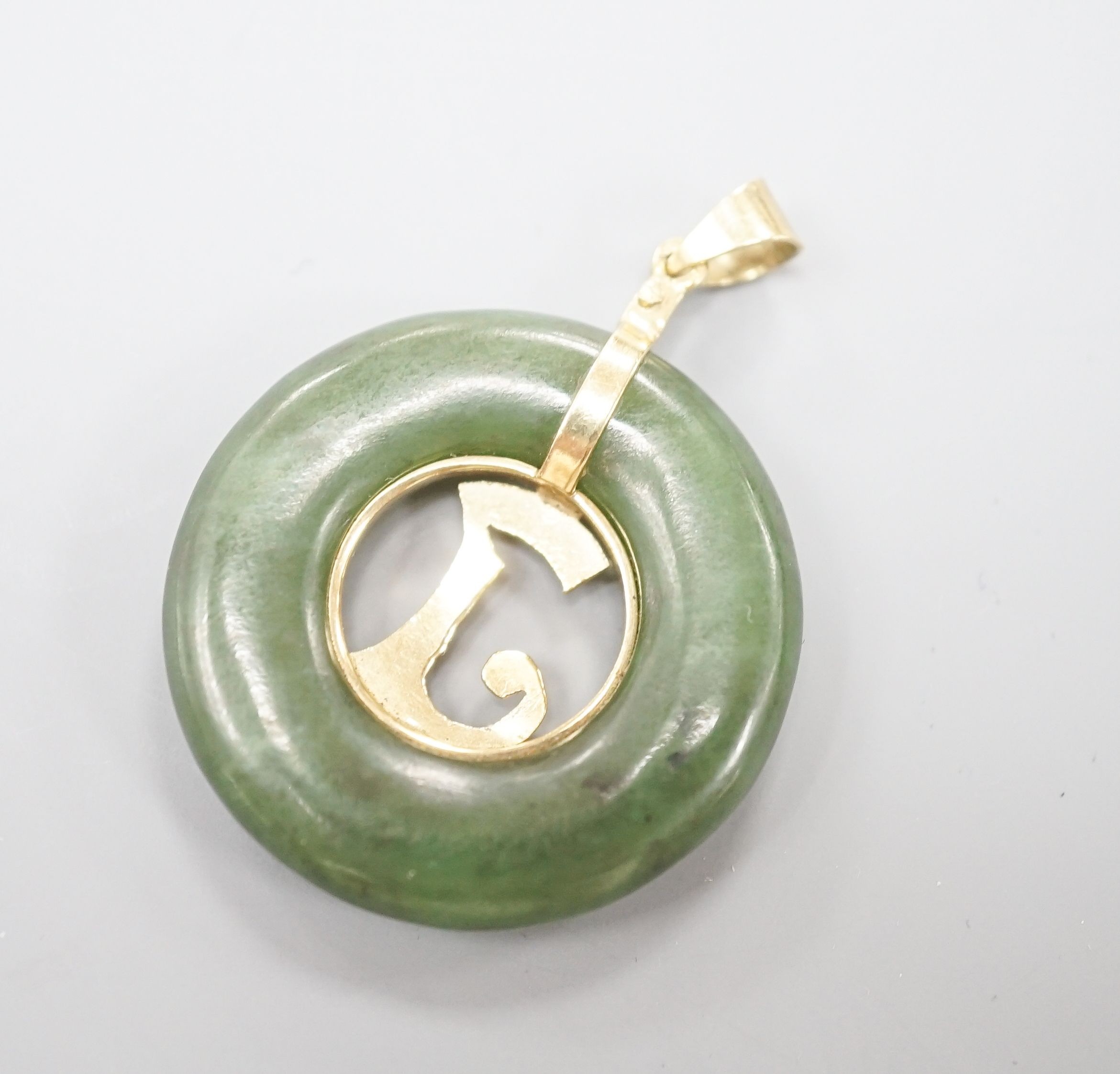 A yellow metal mounted pierced circular nephrite pendant, diameter 29mm, gross weight 8.5 grams.